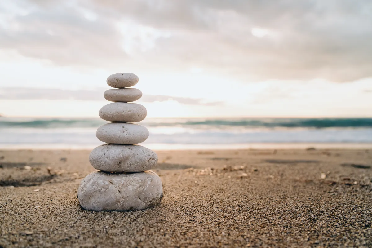 Balanced stones on a sandy beach at sunset — symbolising equilibrium and inner peace